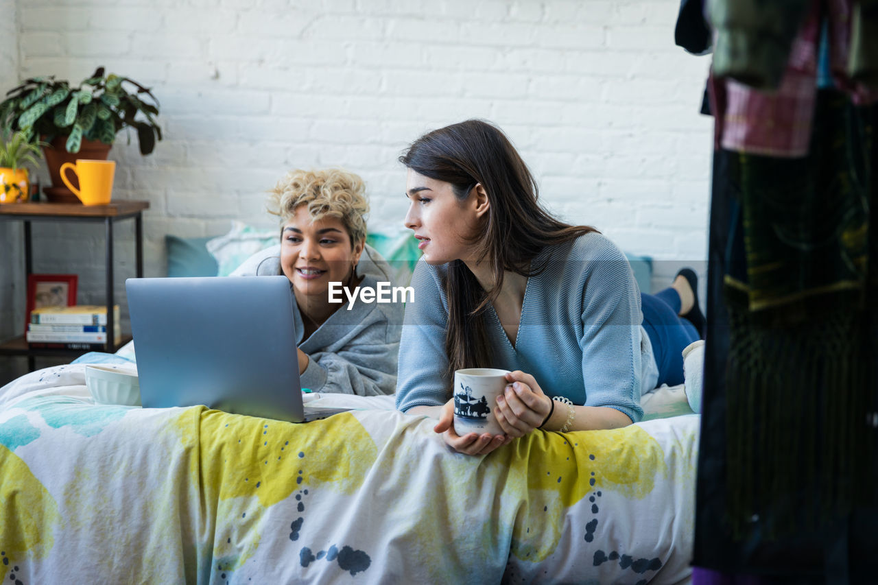 Female friends looking at laptop while relaxing on bed at home