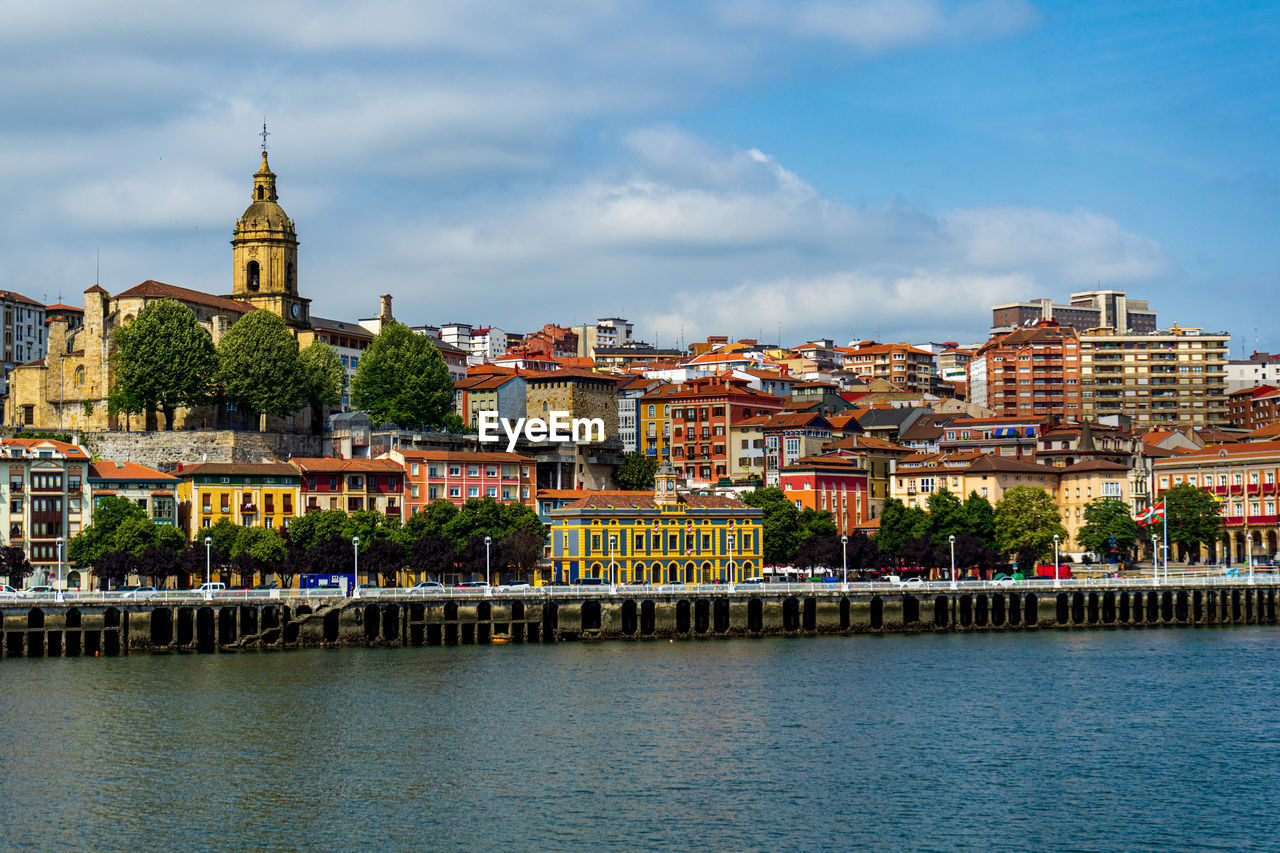 buildings by river against sky in city