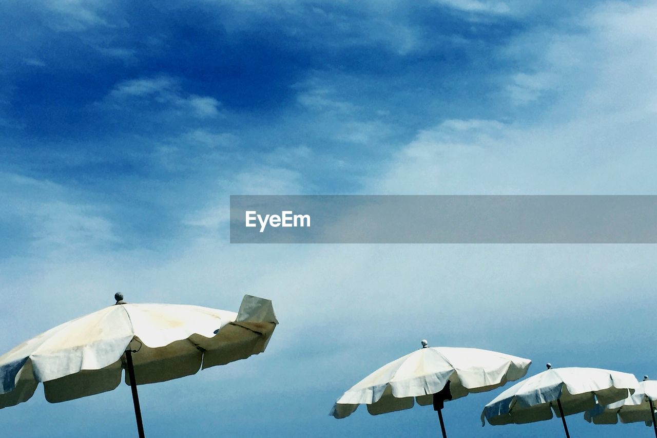 Low angle view of sunshades against cloudy sky