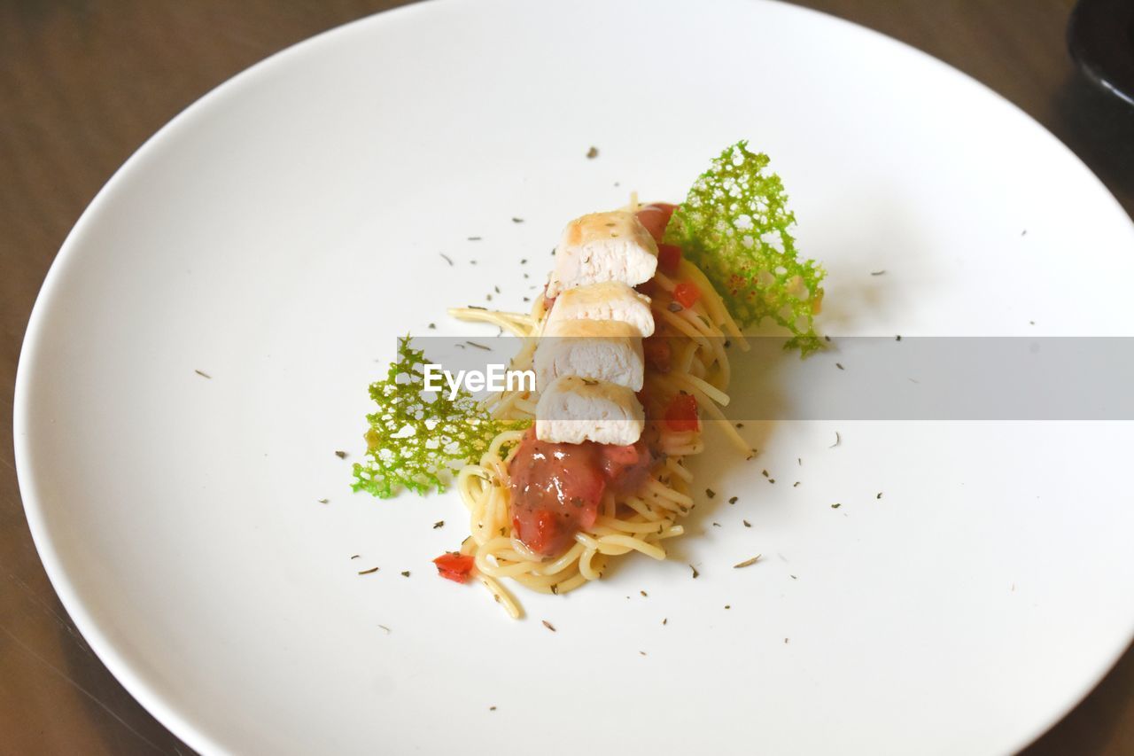Spaghetti bolognese with chicken pan seared , coral tuile garnish