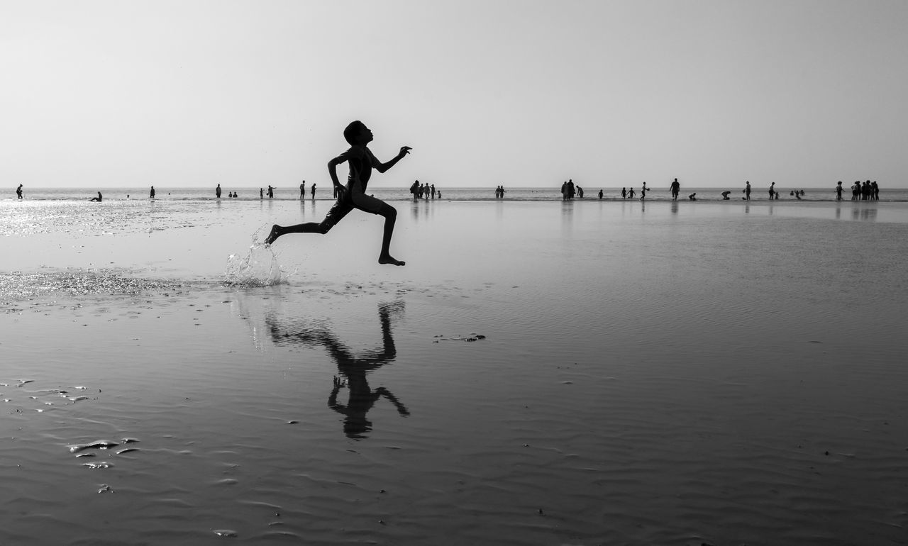 Full length of boy running on sea shore at beach against clear sky