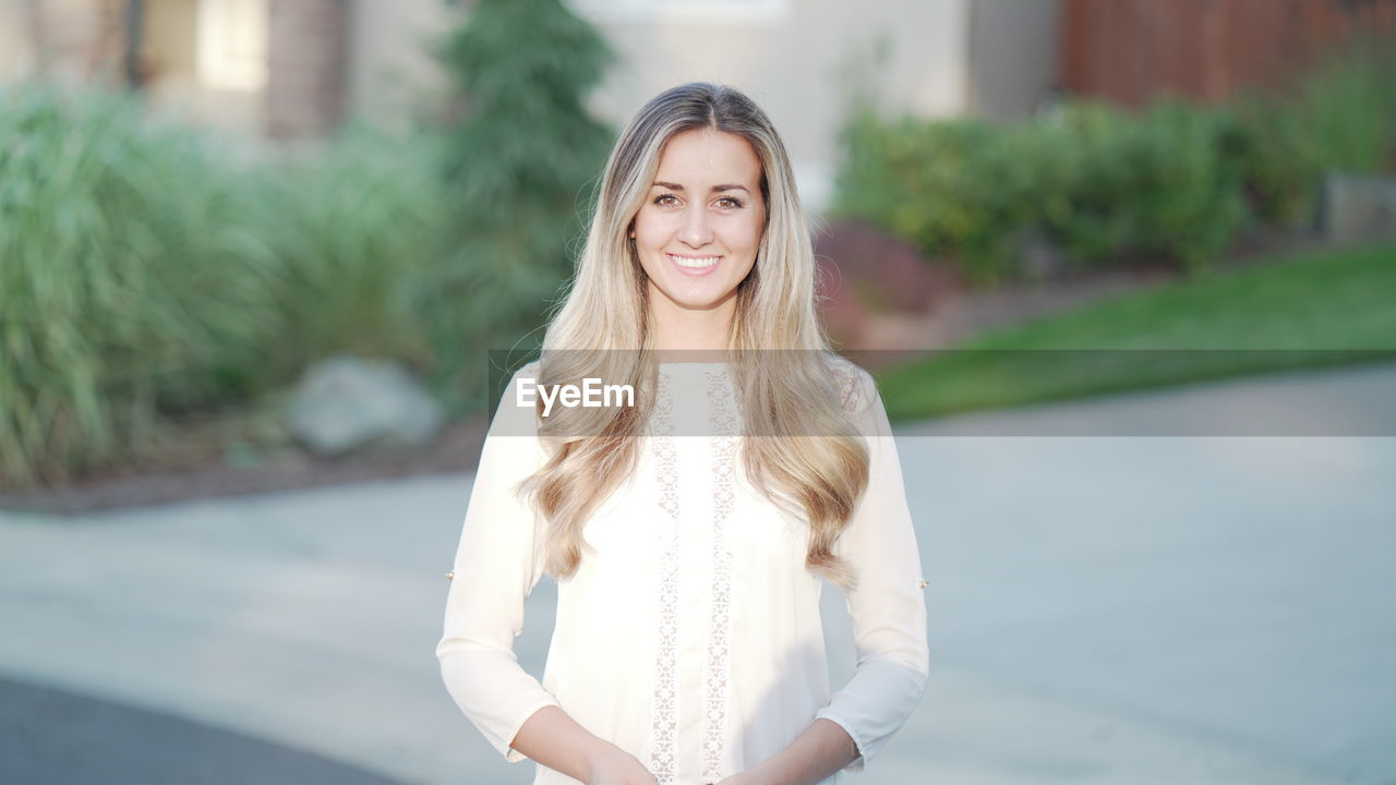 PORTRAIT OF HAPPY YOUNG WOMAN STANDING OUTDOORS