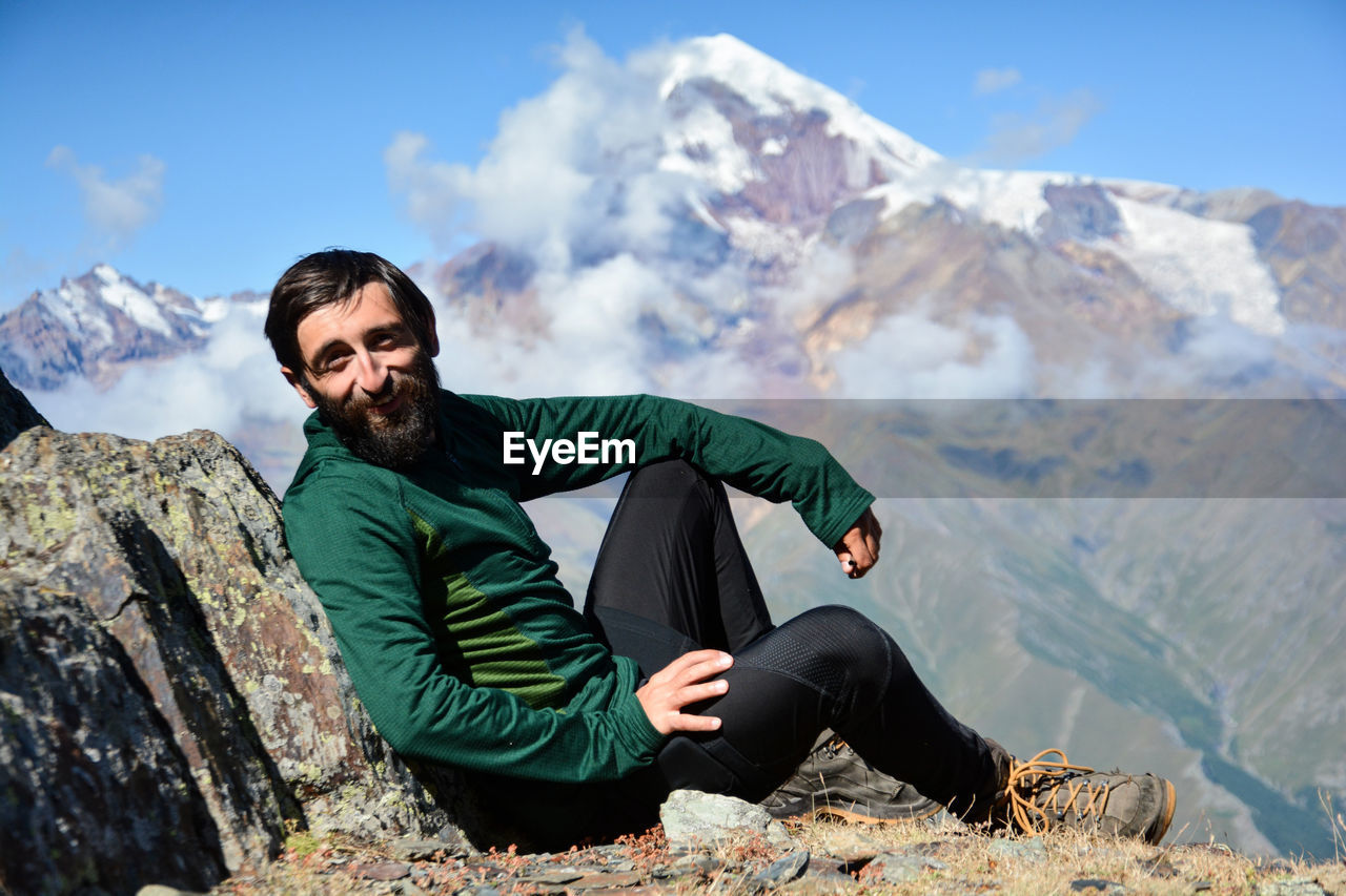 Portrait of man sitting on rock formation against mountain