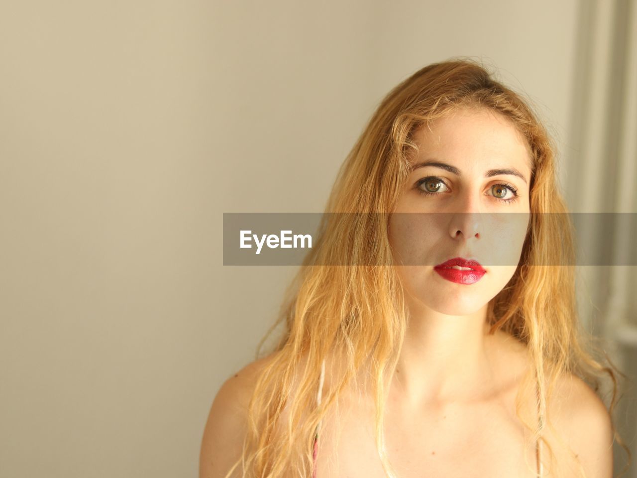 Close-up portrait of young woman standing against wall at home