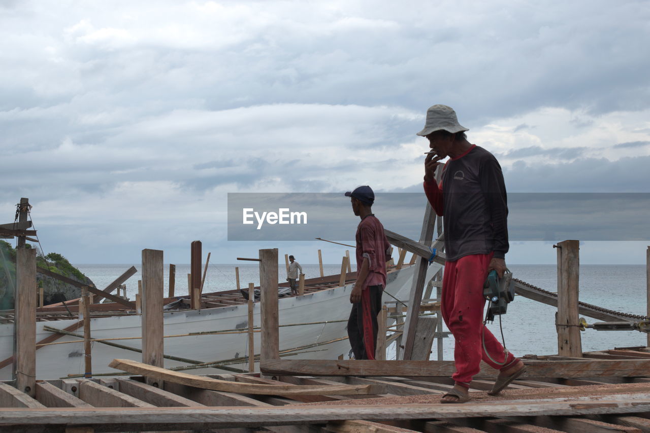 PEOPLE STANDING ON RAILING AGAINST SEA