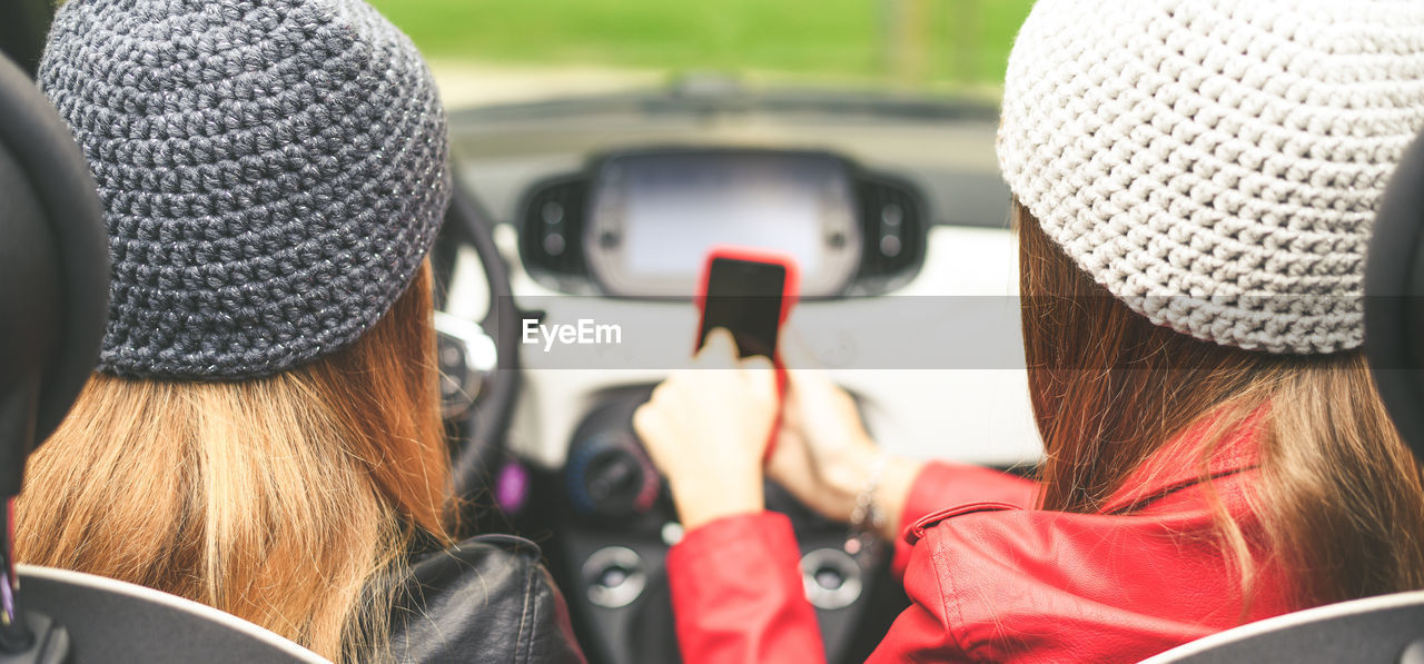 Trendy girls sitting in the car. teen with friend using smartphone. young women enjoying free time