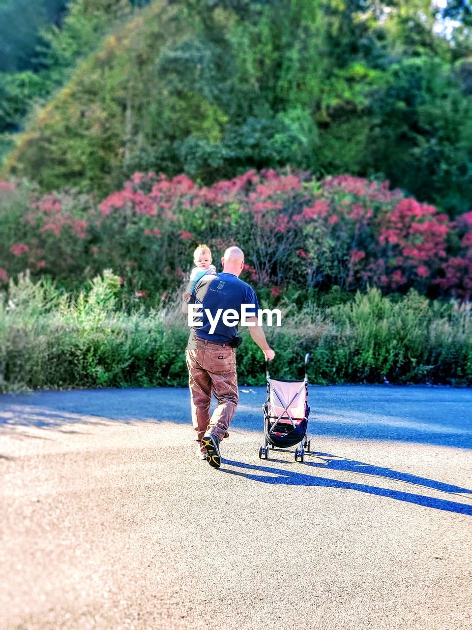 REAR VIEW OF MEN WALKING ON ROAD AGAINST PLANTS