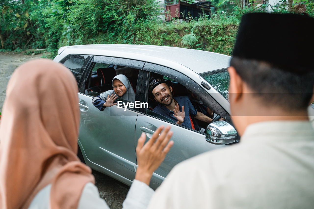 Man driving car while waving at family