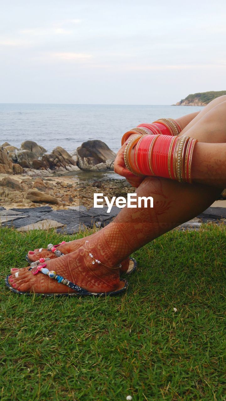 Cropped image of newlywed woman with bangles and henna tattoo sitting at sea shore