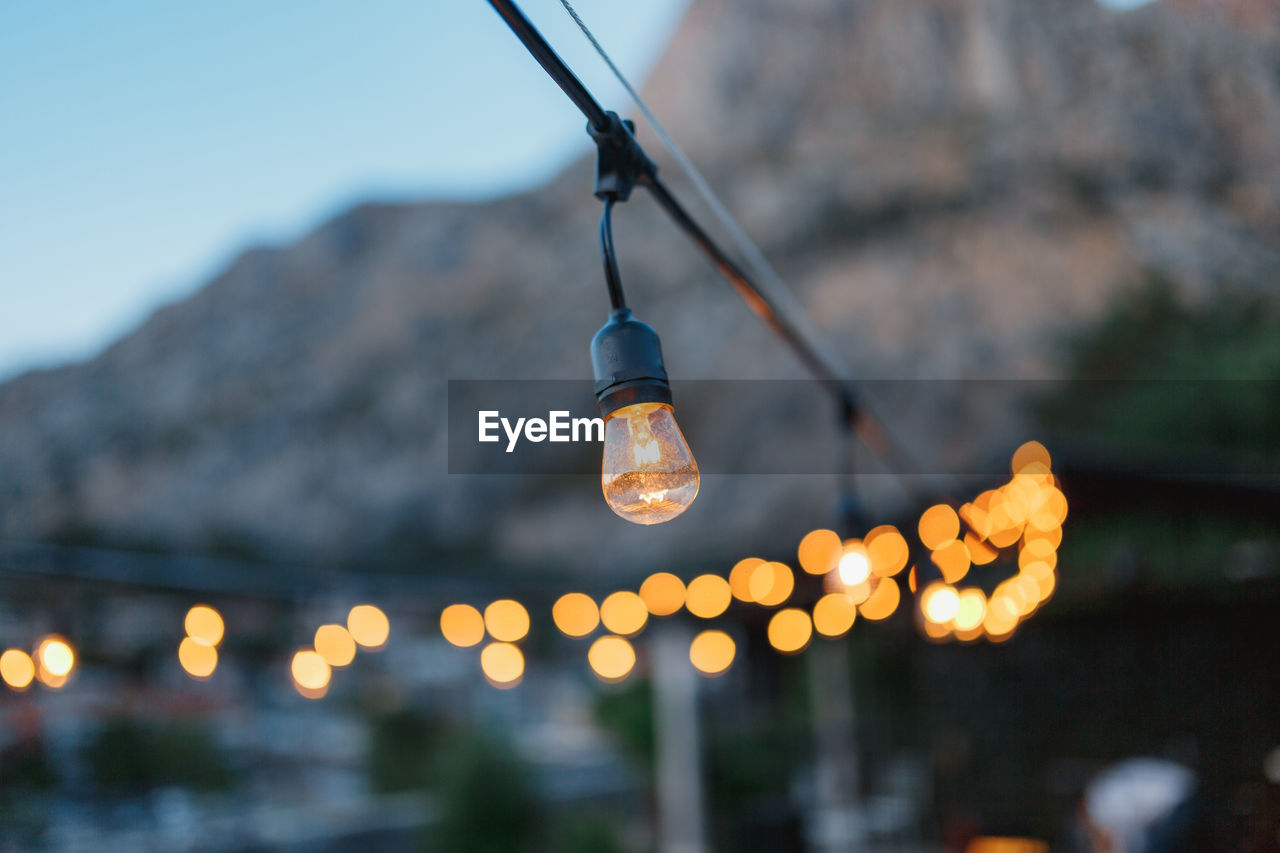 LOW ANGLE VIEW OF ILLUMINATED LIGHT BULBS HANGING AGAINST SKY