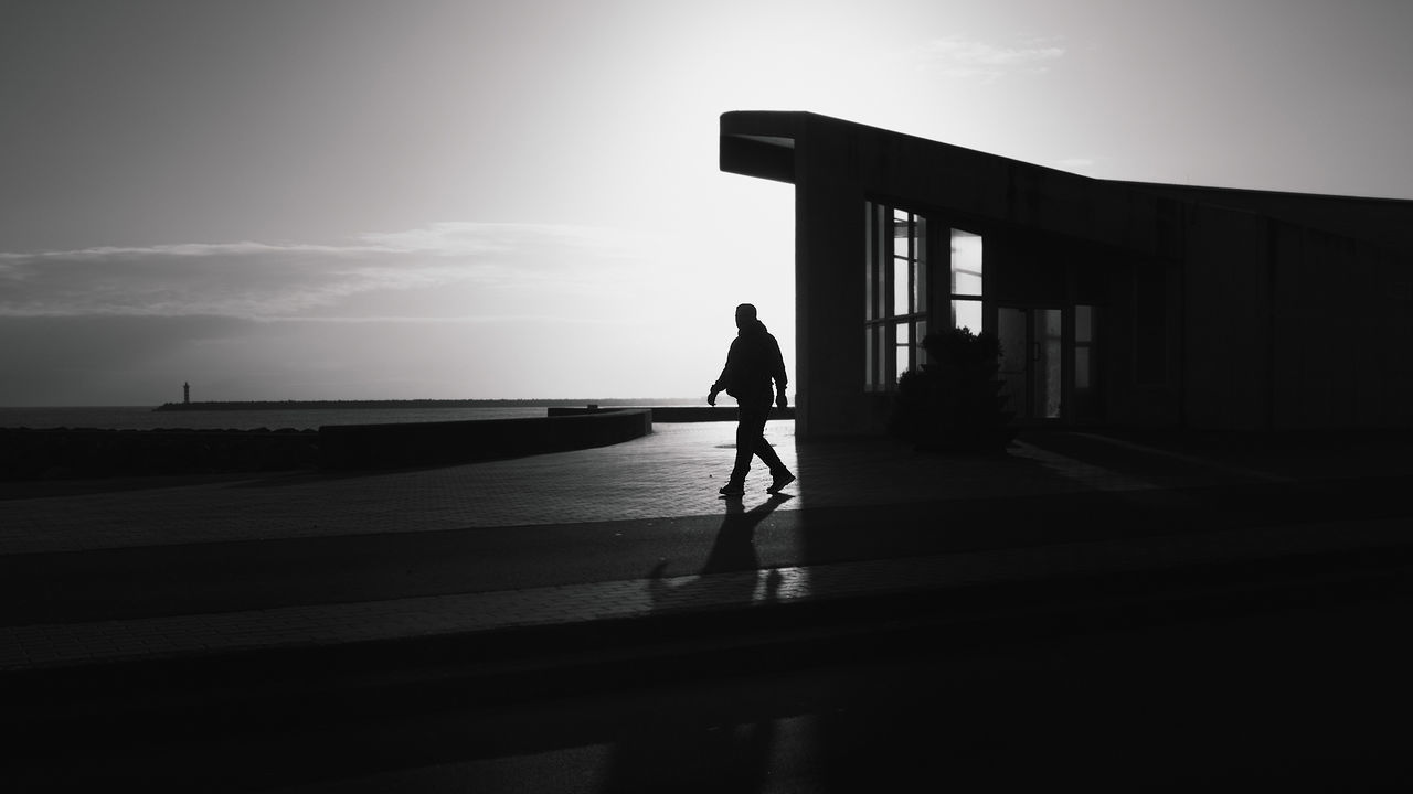 Full length of silhouette man walking on sidewalk against sky