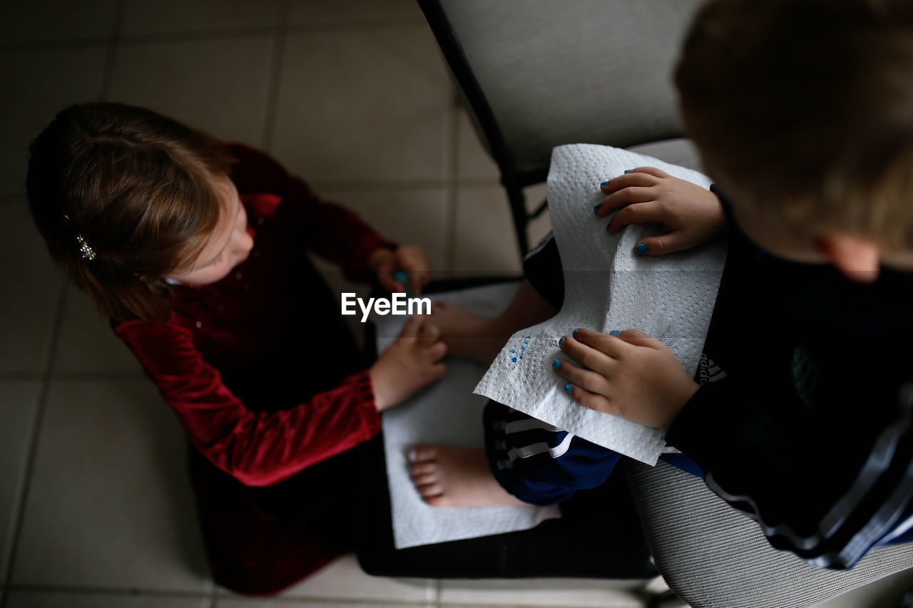 High angle view of sister painting brother's toenails sitting on chair at home