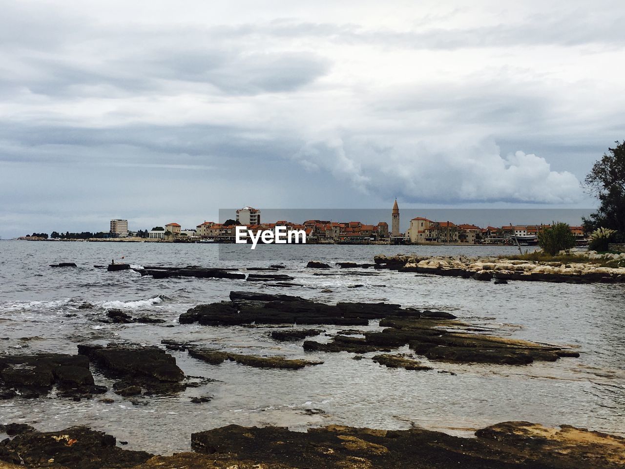 View of city at waterfront against cloudy sky