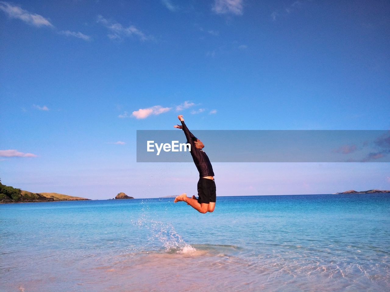 Man jumping on shore at beach against sky