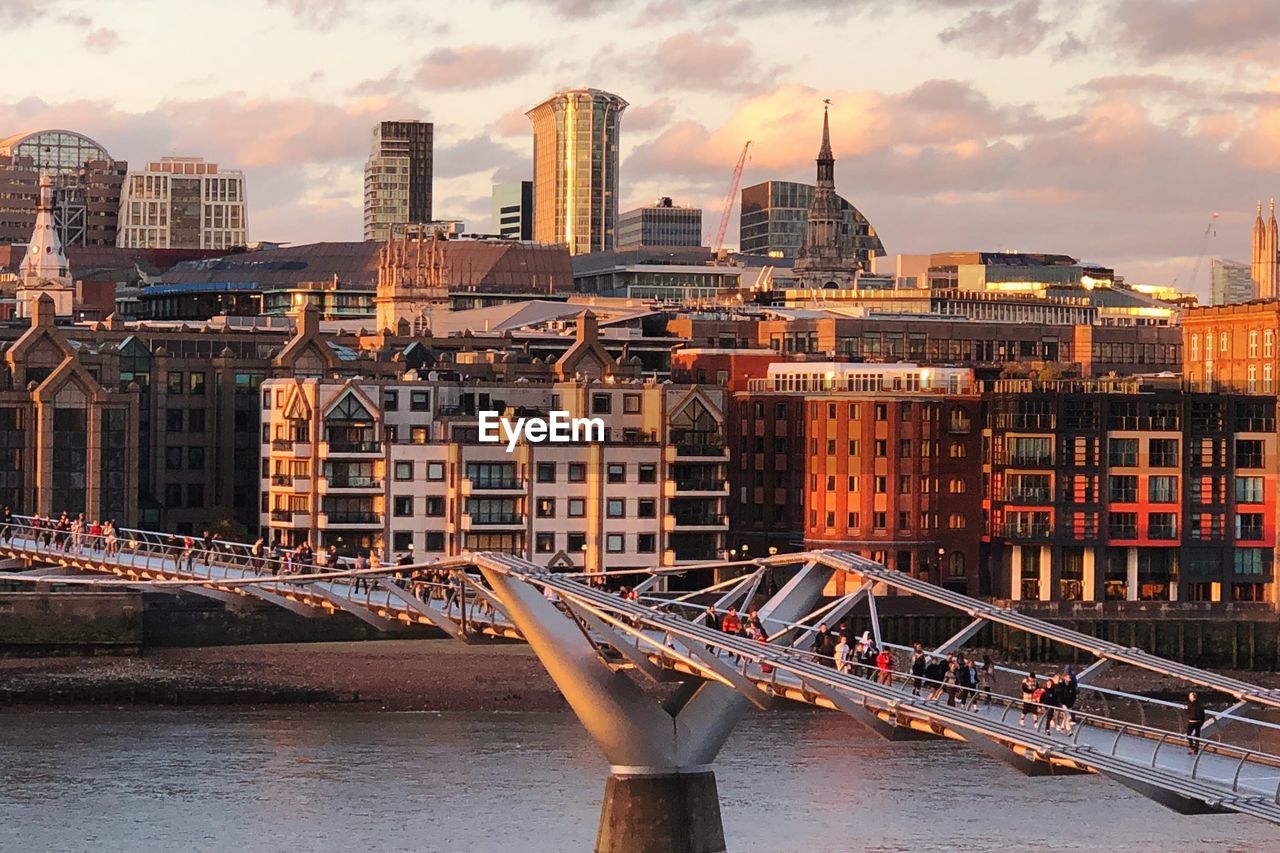Bridge over river against buildings in city at sunset