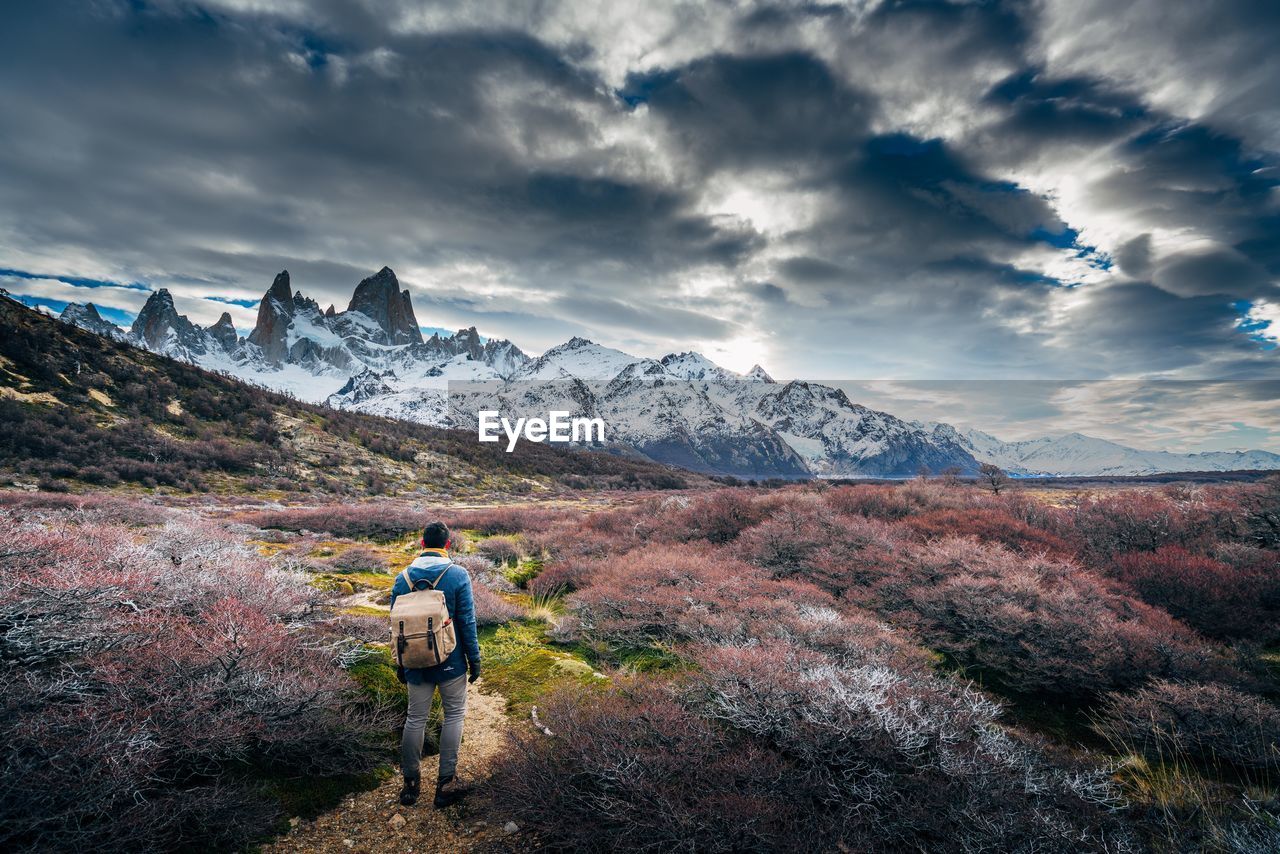 Rear view of man walking on mountain against cloudy sky
