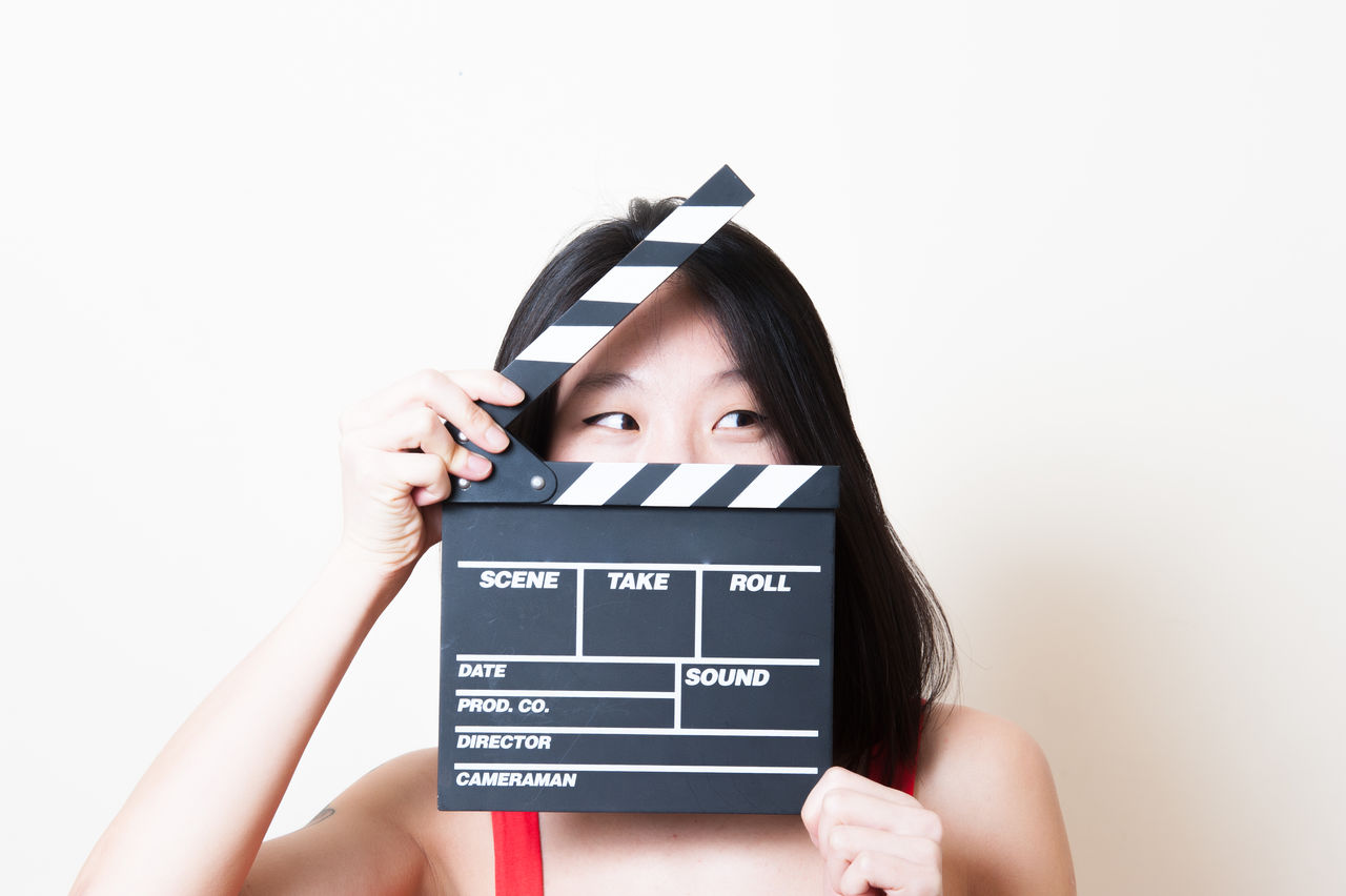 Close-up of young woman holding film slate against white wall at home