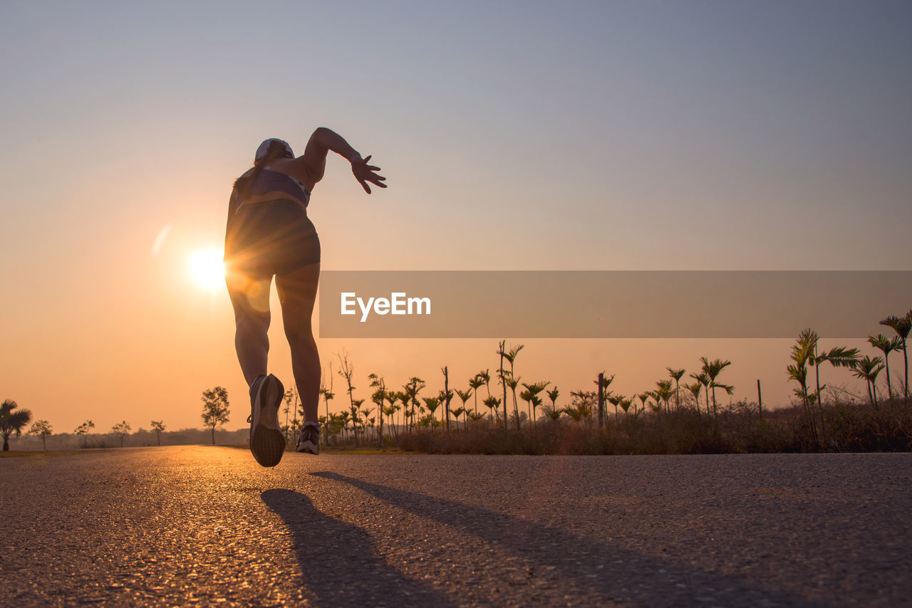 Rear view of woman running on road against sky during sunset