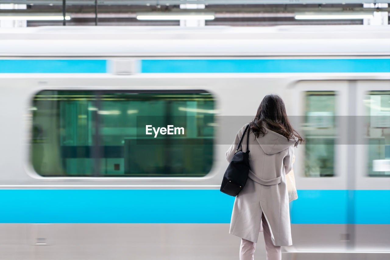 REAR VIEW OF WOMAN STANDING ON TRAIN AT RAILROAD STATION PLATFORM