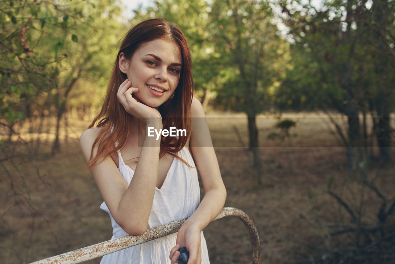 Portrait of smiling young woman against trees