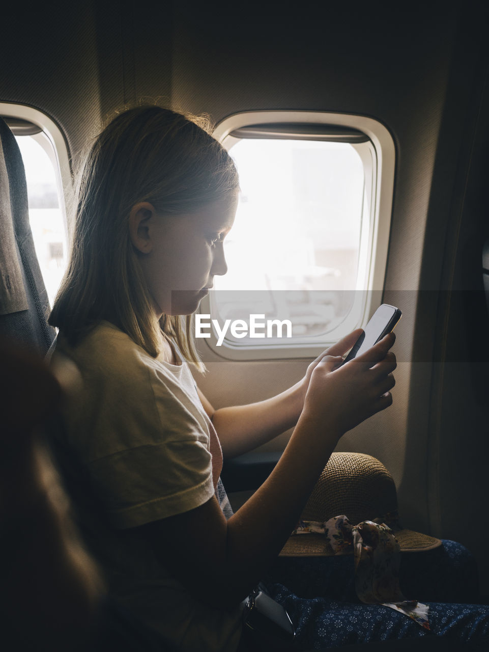 Side view of girl using mobile phone while sitting by airplane window