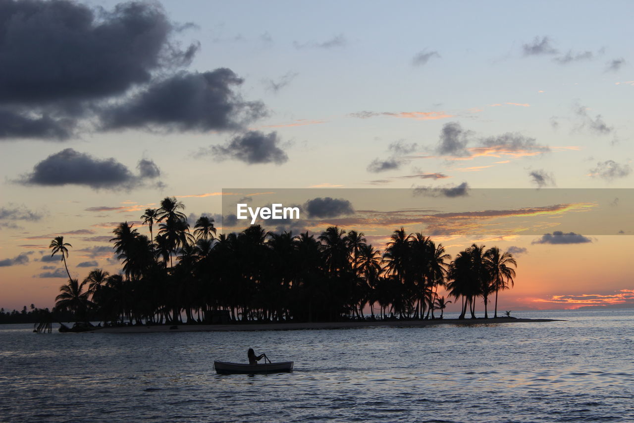 Silhouette of a person paddling against a dreamlike island