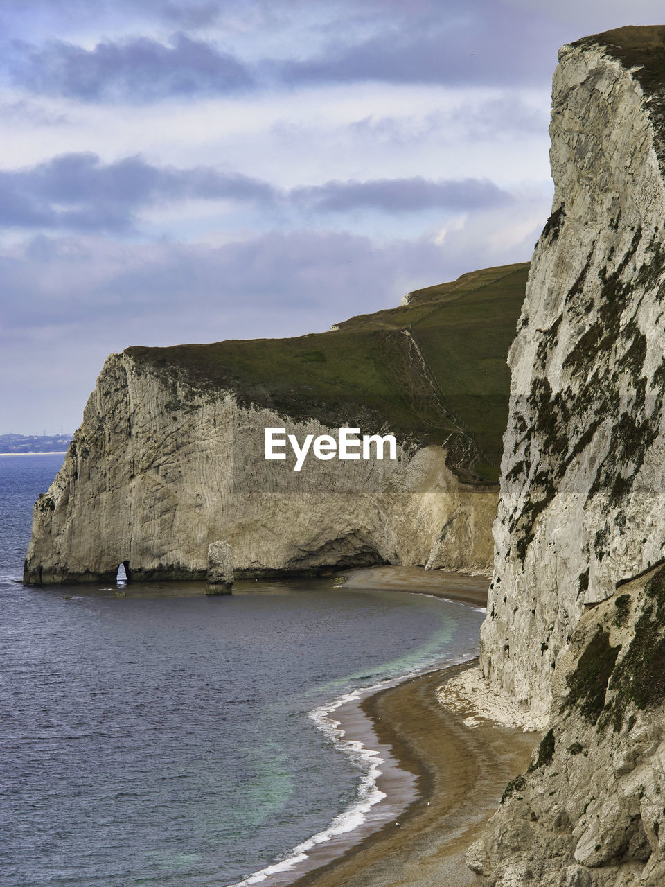 Scenic view of sea by mountain against sky