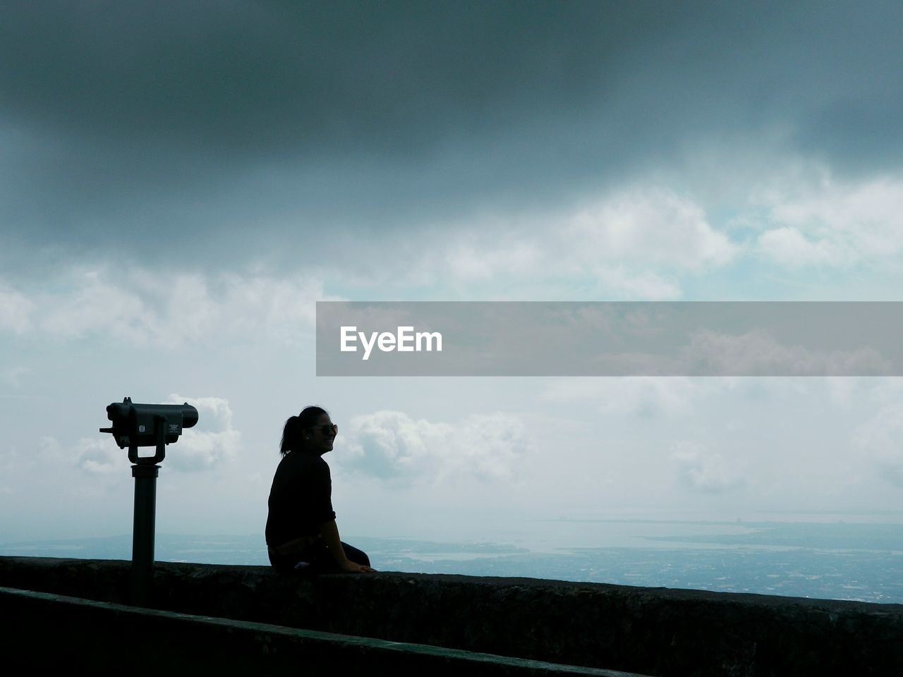 Silhouette of woman sitting at observation point against cloudy sky