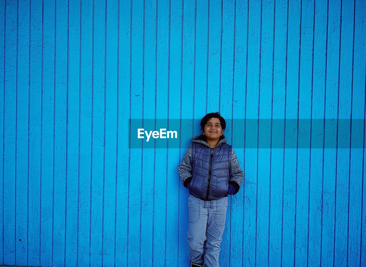 Smiling boy standing against blue wall