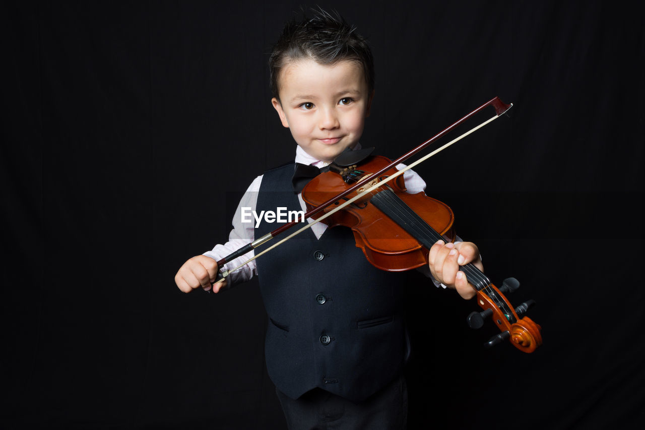 Portrait of boy playing violin against black background