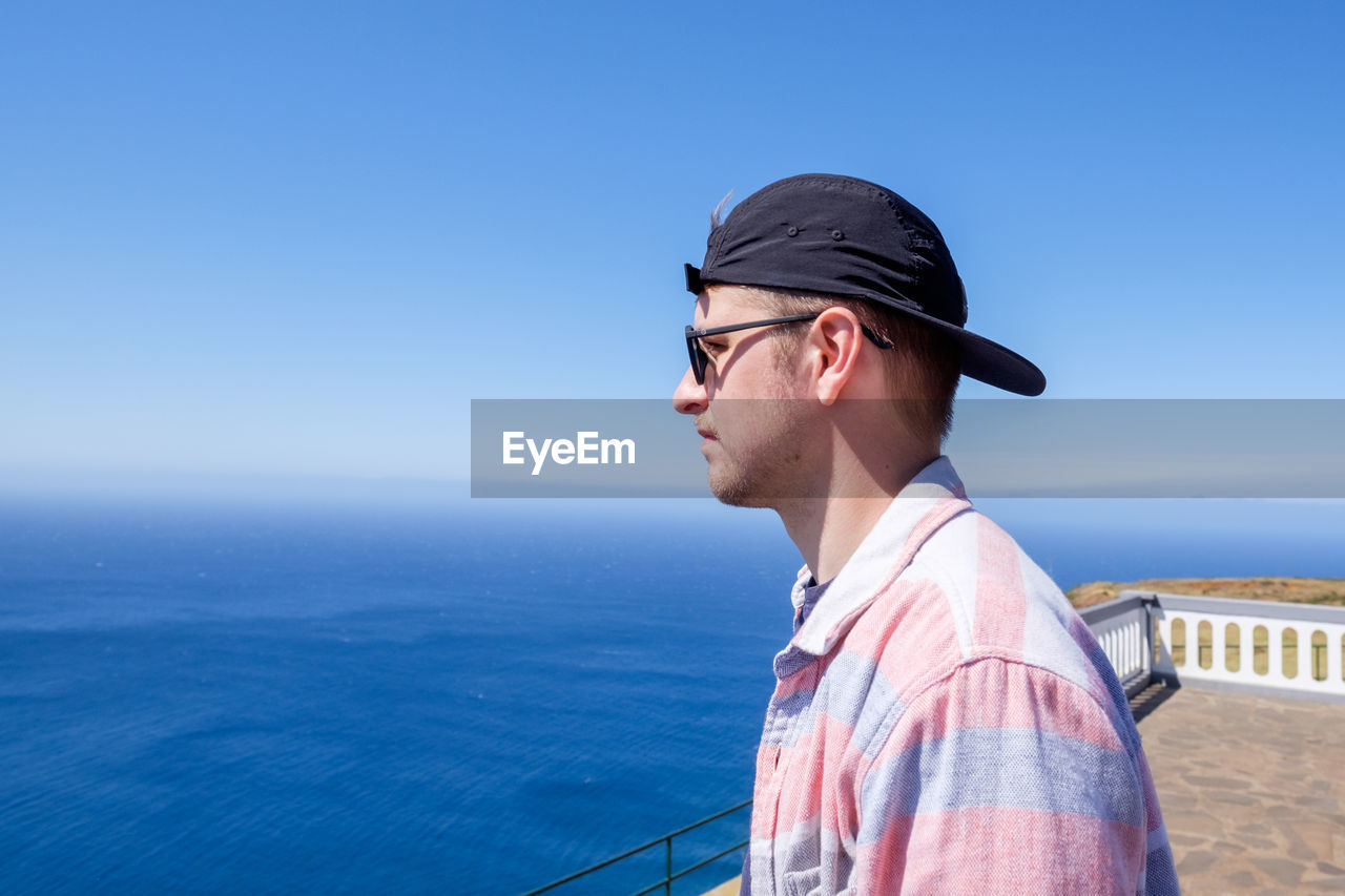 Close-up of young man looking at sea against clear blue sky
