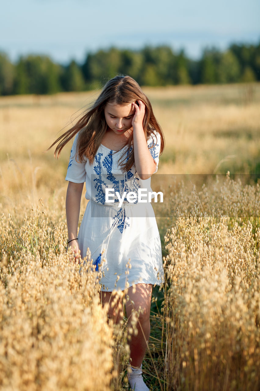 YOUNG WOMAN STANDING ON FIELD DURING SUNRISE