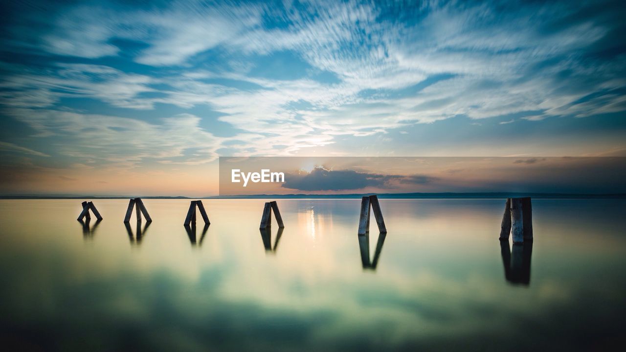 Wooden post in calm lake neusiedl against cloudy sky during sunset