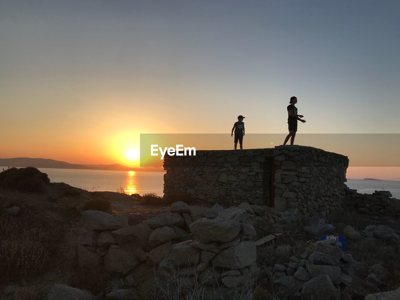 SILHOUETTE PEOPLE ON ROCK DURING SUNSET