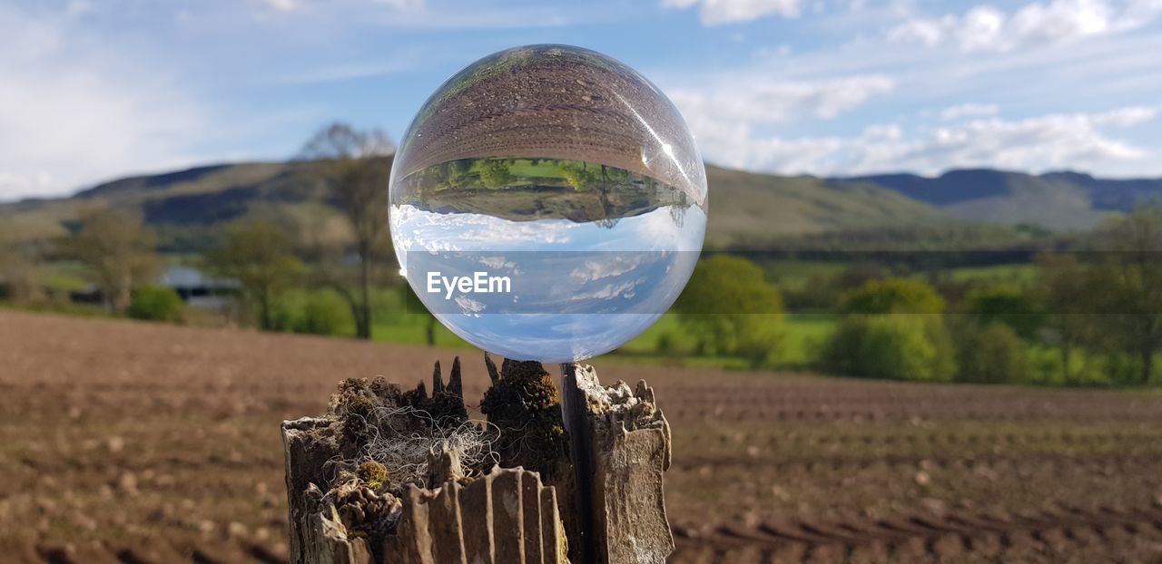 Close-up of glass sphere on wooden posts on field against sky