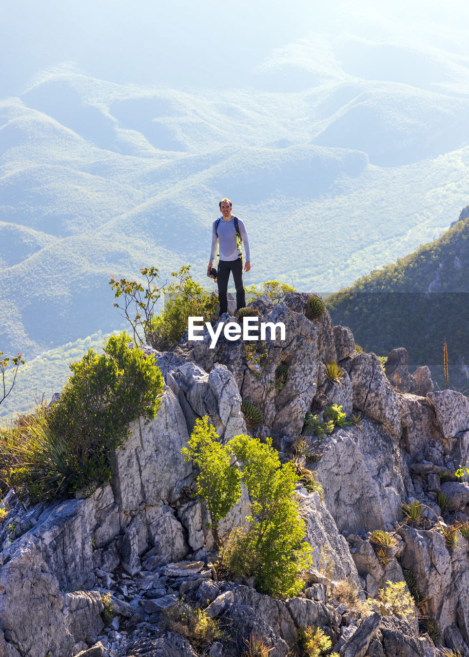 MAN STANDING ON ROCKS AGAINST MOUNTAIN