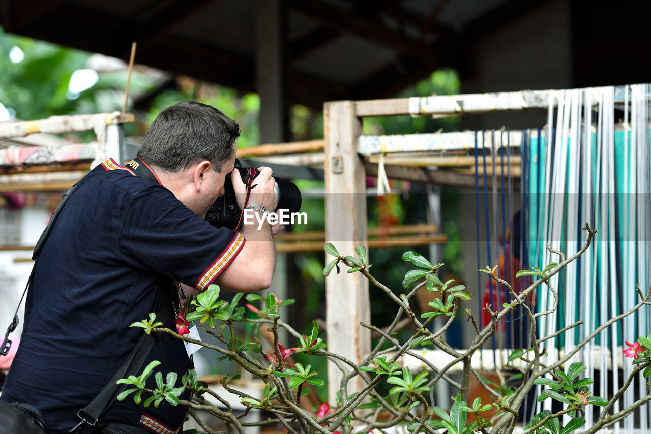 FULL LENGTH OF YOUNG MAN PHOTOGRAPHING THROUGH FENCE