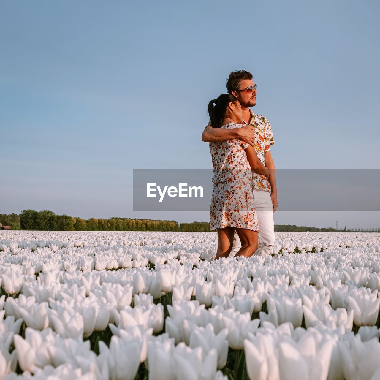 Couple embracing amidst white flowers against sky