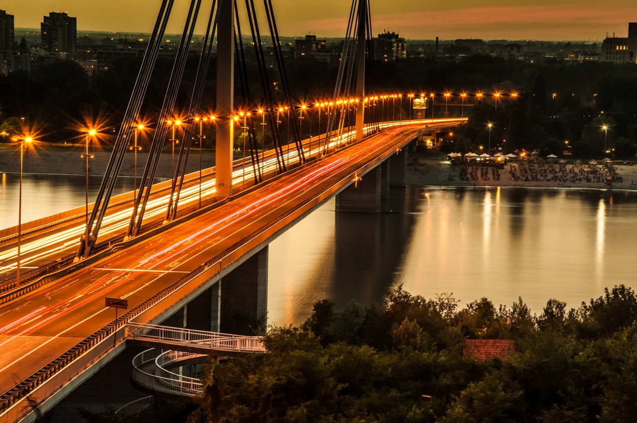 Light trails on bridge in city against sky at night