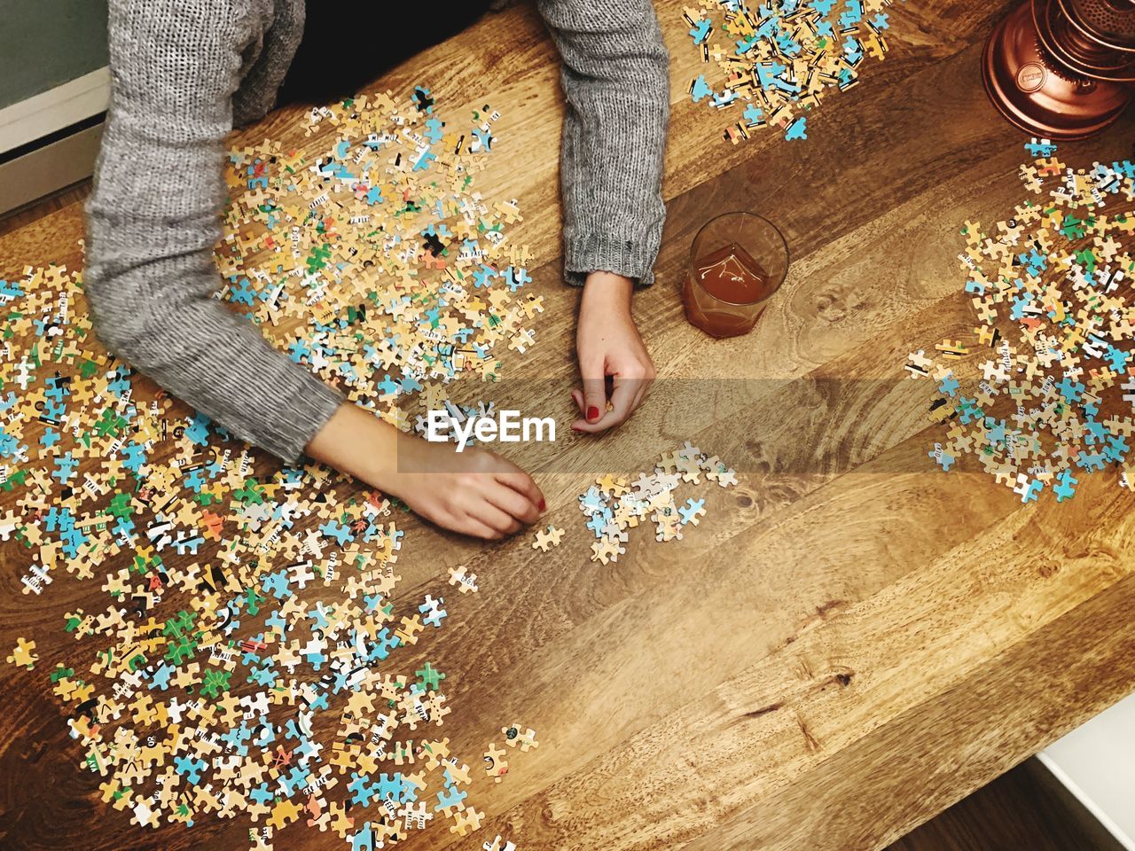 Cropped hands of woman playing jigsaw puzzle on wooden table at home