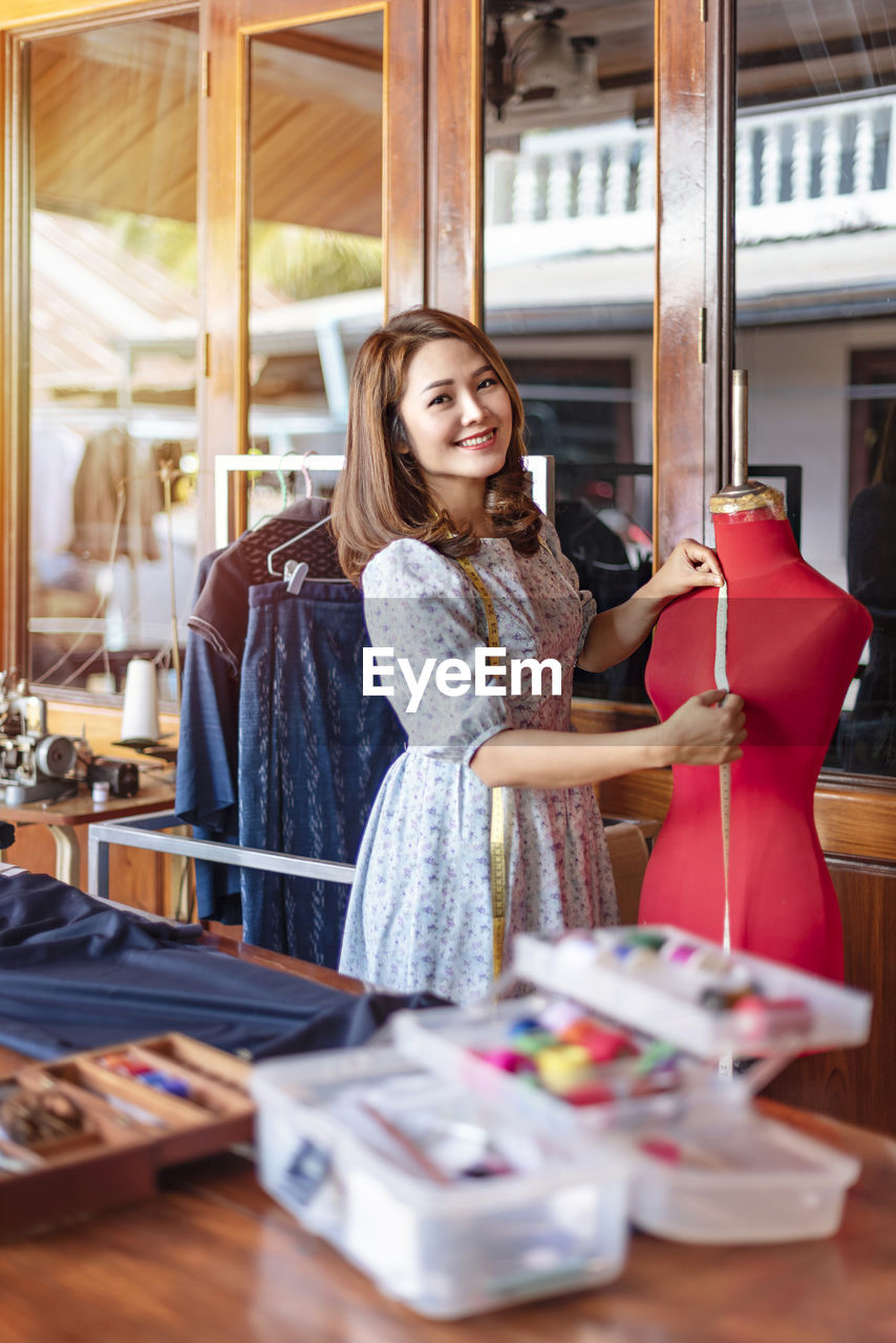 Smiling fashion designer measuring mannequin at fashion studio