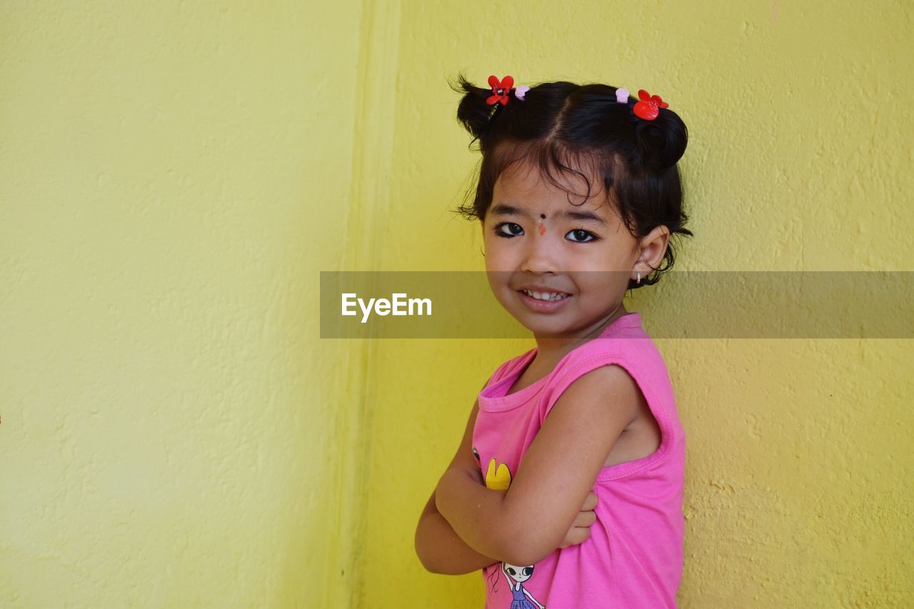 Portrait of smiling girl standing against yellow wall