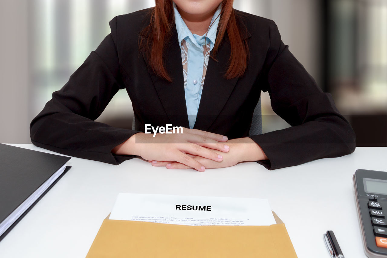 Midsection of businesswoman sitting with resume at desk