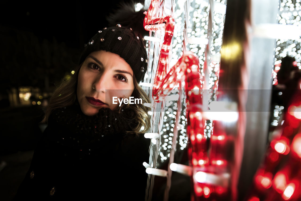 A young girl is posing and looking at the camera next to christmas lig