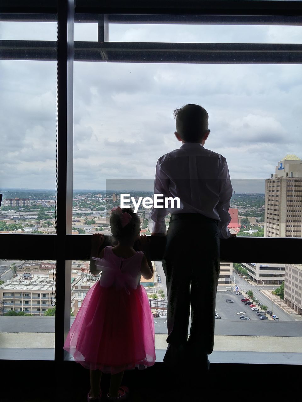 Rear view of siblings looking city through window