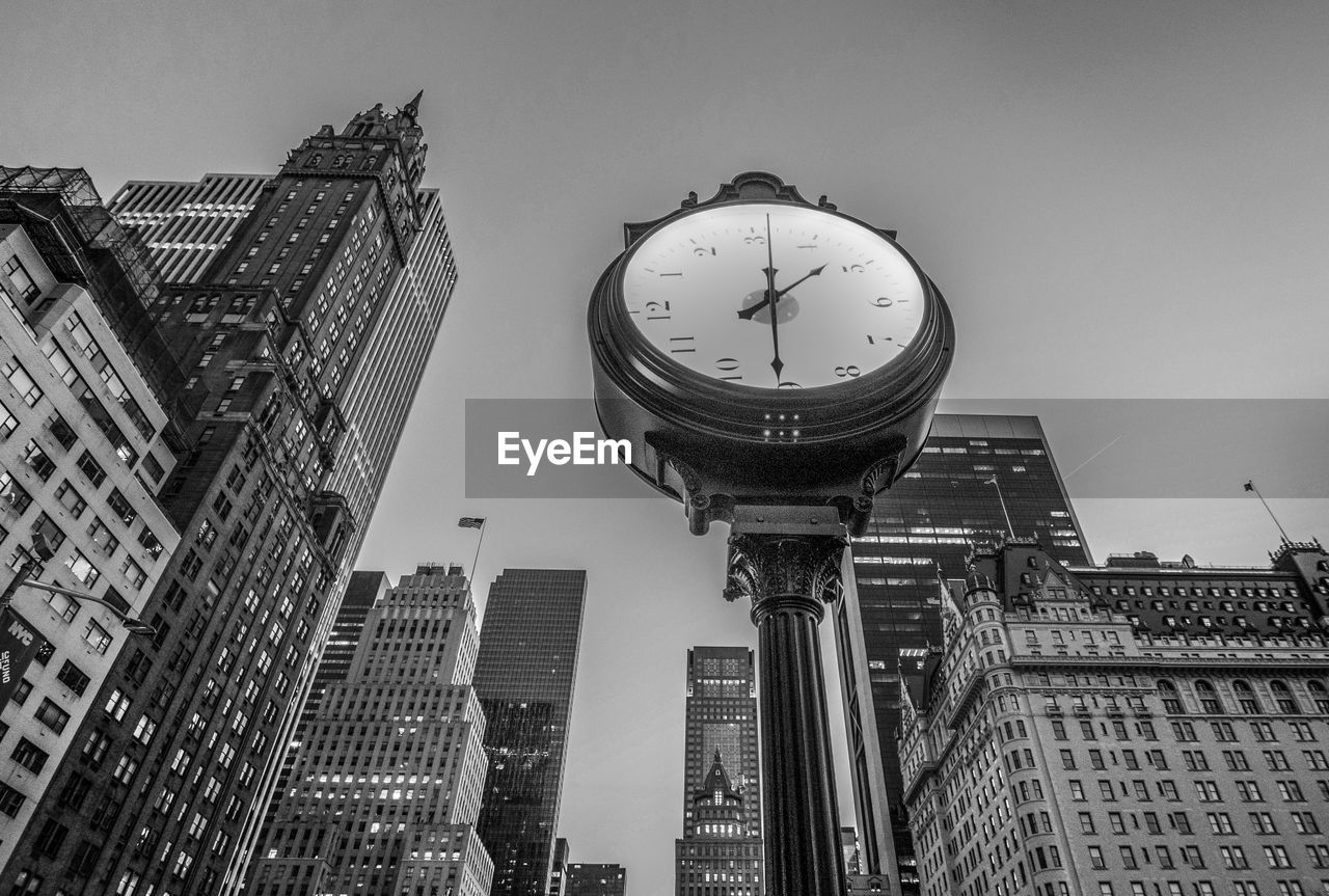 Low angle view of clock against tall buildings