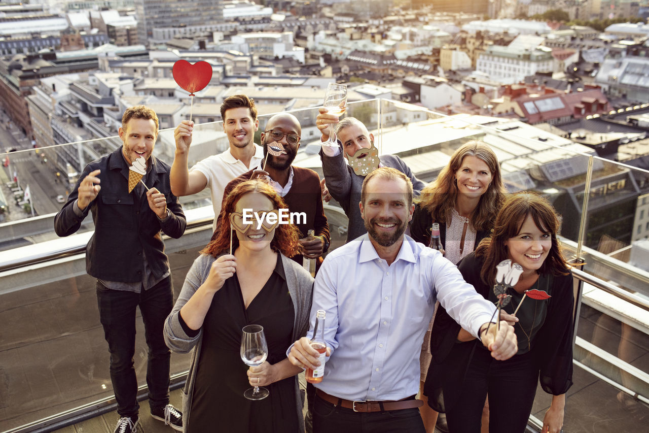 Portrait of cheerful business team with props and drinks enjoying after work party on terrace