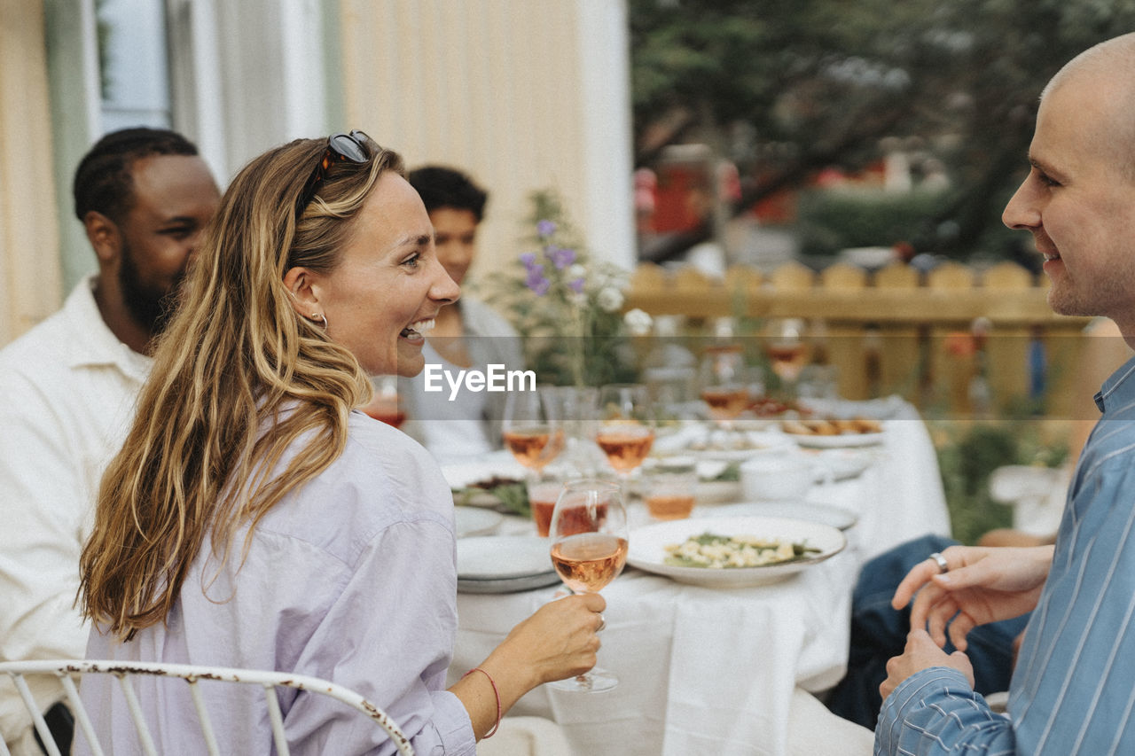 Happy young woman holding wineglass while laughing with male friend during dinner party at cafe