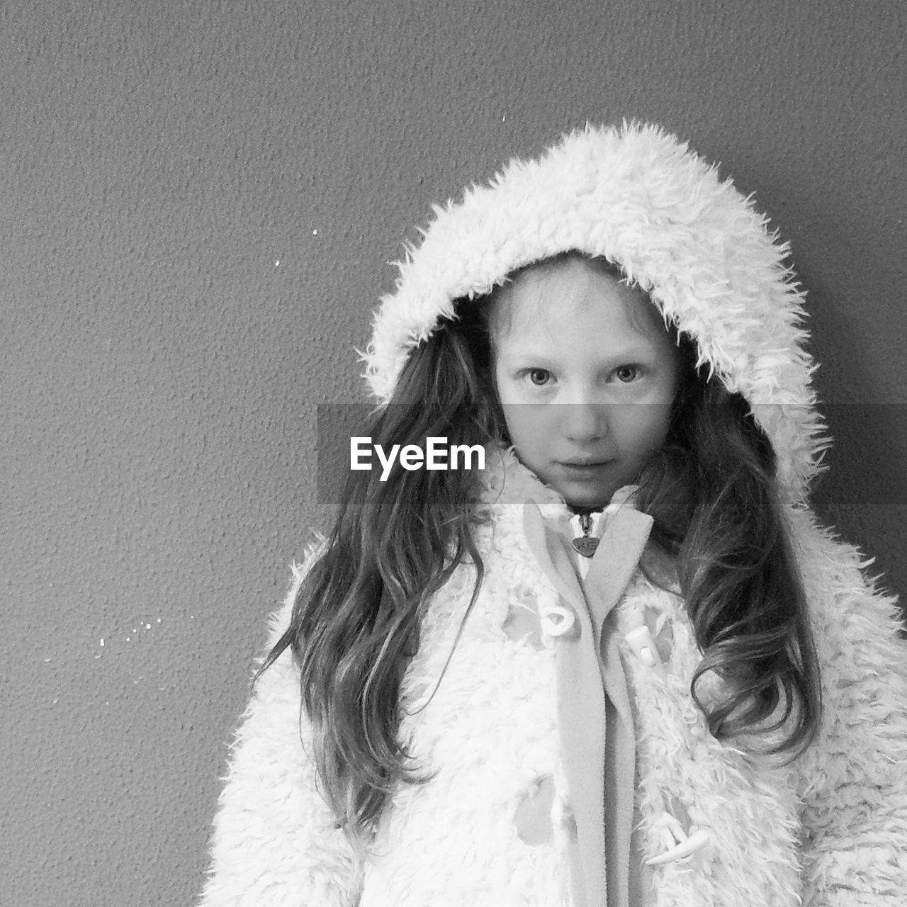 Portrait of girl in fluffy jacket standing by wall