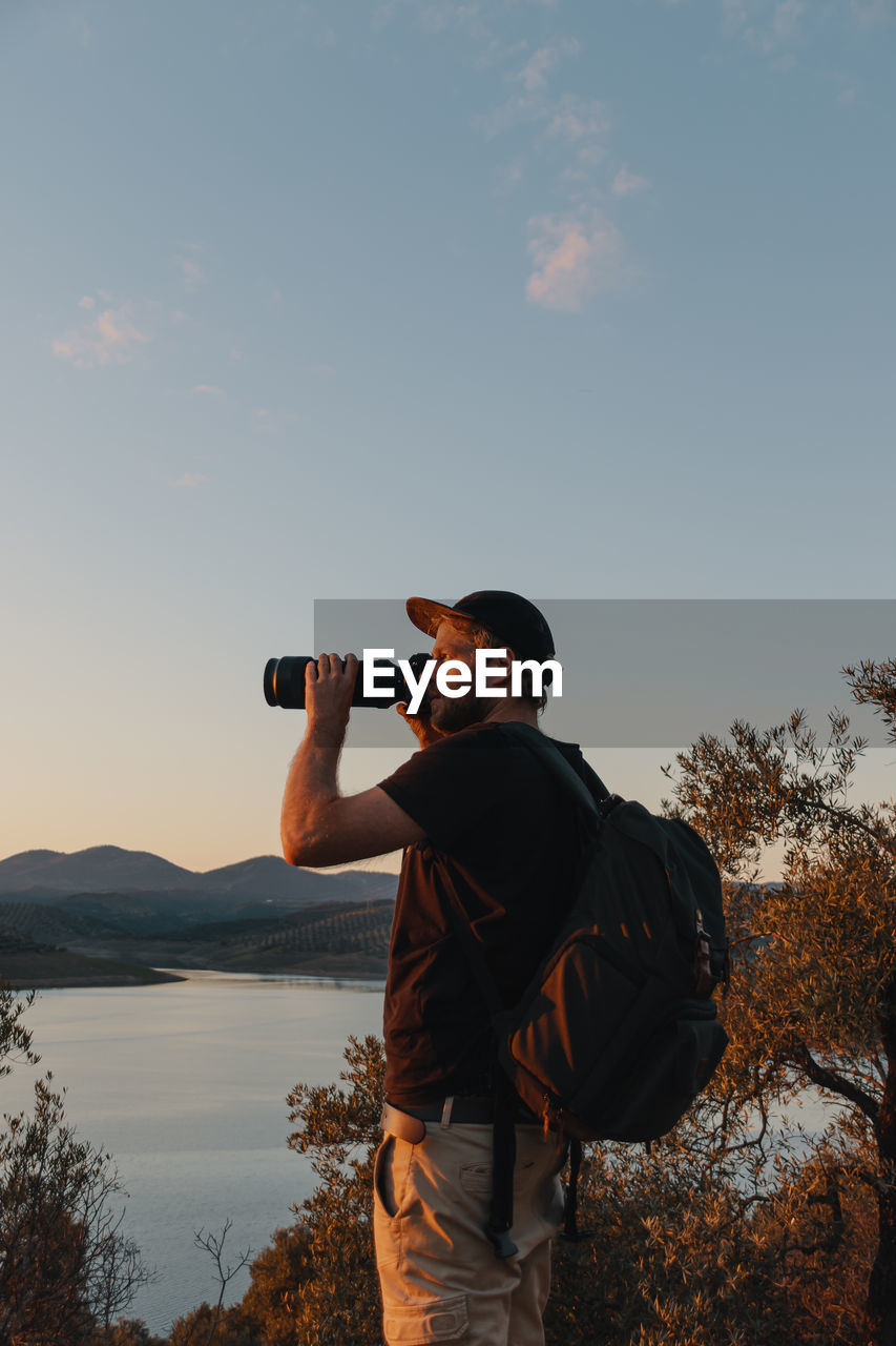 Man photographing against sky at sunset